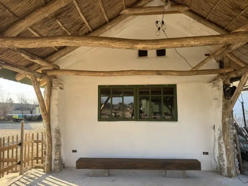 Fereastra veche de aproape 90 de ani, restaurată și vopsită în verde, montată pe latura de nord a casei vechi din 1893, sub o streașină din bușteni și stuf